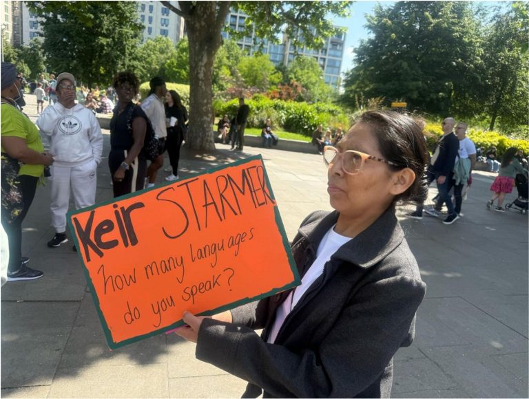 Woman in park holding sign that reads: "Keir Starmer, how many languages do you speak?".