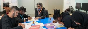 ELATT support worker giving one-to-one help to a small group of students working together at a table in a Sixth Form classroom
