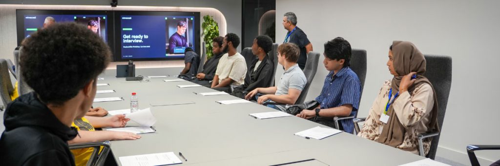 A large conference room with many people at a table watching a presentation on employment and career guidance.